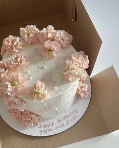 a white cake with pink flowers on top in a box