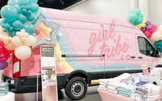 a pink van with balloons and stars on the side is parked in a showroom