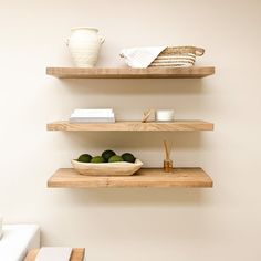 two wooden shelves with bowls and plates on them in a room that has white walls