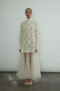 a woman standing in front of a white wall wearing a dress with sheer tulle