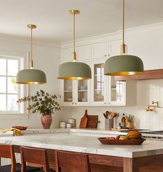 three lights hanging over a kitchen island with wooden chairs and counter top in front of it