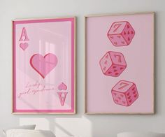 two pink framed pictures with hearts and dices on them in a white room next to a bed