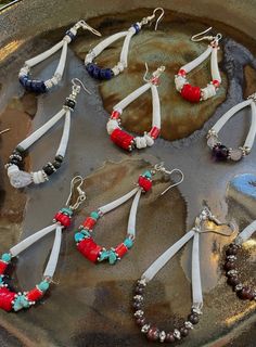 several different colored beads are hanging from earrings in a bowl on a table with rocks