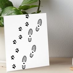 a white card with black footprints on it next to a potted plant