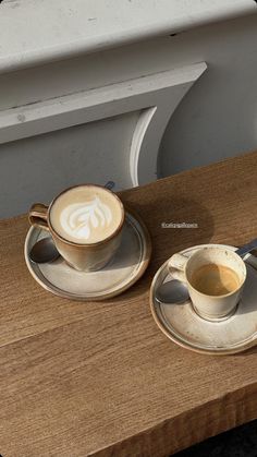 two coffee cups with saucers sitting on a wooden table next to an empty cup