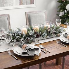 the table is set with silverware, candles and greenery