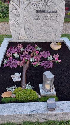 a small tree is placed in the middle of a grave with flowers and rocks around it