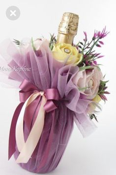 a bottle of champagne and flowers in a purple vase with ribbon tied around the top