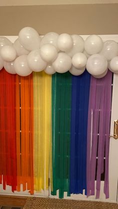 balloons and streamers are hanging from the ceiling in front of a rainbow - colored curtain