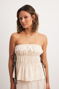 This bandeau top features a lining and a chiffon layer. It has elasticized drawstrings with self-tie knots. Chic Bandeau Tube Top For Brunch, Chic Off-shoulder Smocked Bodice Tube Top, Chic Off-shoulder Smocked Tube Top, Chic White Smocked Bodice Tube Top, Chic Smocked Bodice Tube Top For Day Out, Chic Bandeau Tube Top With Smocked Bodice, White Ruched Bandeau Tube Top, Spring Strapless Tube Top With Tie Back, Strapless Tube Top With Tie Back For Spring