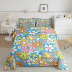 a bed with colorful flowers on it in a room next to a white table and chair