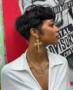 a woman standing in front of a graffiti wall wearing earrings and a white shirt with gold cross pendants on her neck