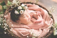 a baby is sleeping in a basket with flowers on her head