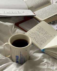 a cup of coffee sitting on top of a bed next to two open book's