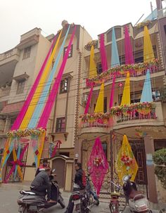 people riding motorcycles and scooters in front of a building decorated with colorful ribbons