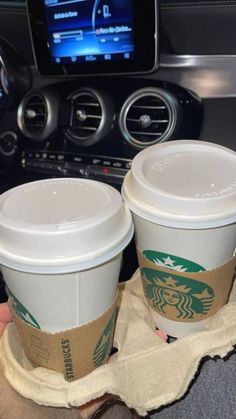 two cups of starbucks coffee sitting on top of a cloth in front of a car radio