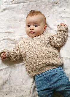 a baby laying on top of a bed wearing a sweater