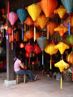 a woman sitting on a bench in front of many colorful lanterns hanging from the ceiling