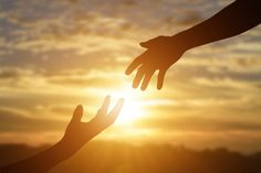 two hands reaching towards each other in front of the sun