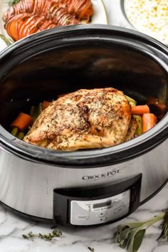 a slow cooker with chicken, carrots and other food in it on a marble counter top