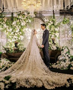 a bride and groom standing in front of an elaborate floral backdrop with chandeliers