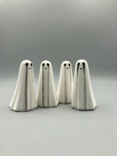 three white ghost figurines sitting next to each other on a gray surface with one in the middle