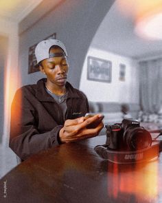 a man sitting at a table looking at his cell phone while holding a camera in one hand