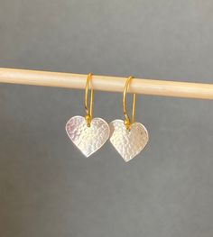 "Simple yet stylish handmade sterling silver and gold vermeil dangle earrings featuring a beautiful hand hammered heart. The heart is suspended from a french style 24k gold vermeil ear wire. Vermeil is a thick coat of 24 karat gold on solid sterling silver. The heart has been given a beautiful dimpled texture that catches the light. Lovingly designed and made by hand in the UK. Lightweight and comfortable to wear. They will add a lovely touch to any outfit and will make an ideal birthday or anni Nickel-free Gold Heart Earrings In Sterling Silver, Gold Sterling Silver Earrings With Heart Charm, Gold Sterling Silver Heart Earrings For Anniversary, Gold Sterling Silver Heart Earrings As Gift For Her, Gold Sterling Silver Dangle Heart Earrings, Gold Sterling Silver Heart Dangle Earrings, Dainty Handmade Gold Heart Earrings, Dainty Handmade Heart Earrings For Anniversary, Handmade Yellow Gold Heart Earrings