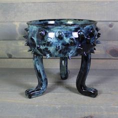 a black and blue ceramic planter with spikes on it's legs sitting on a wooden surface