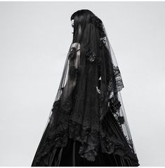 a woman wearing a black veil and dress with flowers on the skirt is standing in front of a gray sky