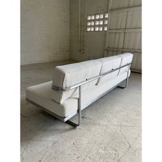 a white couch sitting on top of a metal frame in an empty room next to a brick wall