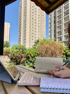 a woman sitting at a table with a laptop and notebook in front of her, writing