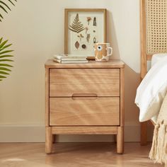 a nightstand with two drawers and a coffee mug on it, next to a bed