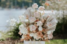 a vase filled with lots of flowers sitting on top of a grass covered field next to water