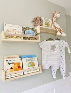 two wooden shelves holding books and baby's clothing on top of each shelf, with a stuffed giraffe hanging from the wall