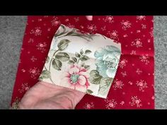 someone's hand on top of a red and white flowered cloth with flowers