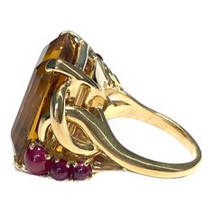 Crafted in 14K yellow gold, the ring features a large rectangular cut citrine solitaire accented by three round ruby cabochons on each side. Citrine: 25 ct. 6 Rubies: 1.60ctw. Measurements: Front: 21.5 mm H x 25 mm W x 12.5 mm D Weight: 26.2 grams Size: 8.5 (sizable) Marked: 14K Luxury Rectangular Ruby Ring, Gold Rectangular Amethyst Ring For Formal Occasions, Rectangular Ruby Ring In Gold, Formal Multi-stone Rectangular Ring, Gold Multi-stone Rectangular Ring, Gold Three Stone Topaz Ring For Formal Occasions, Formal Gold Three Stone Topaz Ring, Formal Gold Three-stone Topaz Ring, Three Stone Gold Topaz Ring For Formal Occasions