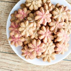 a white plate topped with cookies covered in pink sprinkles on top of a wooden table