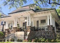 a white house with columns and pillars on the front porch is surrounded by greenery