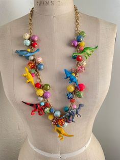 a mannequin wearing a necklace with toy dinosaurs on it's neck and beads