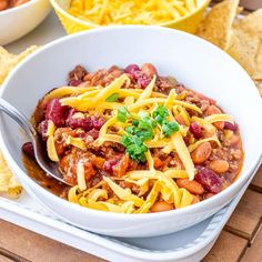 a white bowl filled with chili and cheese next to tortilla chips on a table