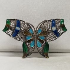 Vintage Sterling and Enameled Filigree Butterfly Brooch. Not marked but tested positive as Sterling. Weighs 0.21 ozt.  Are these stones real or fake? Aside from diamonds, we do not know if any gemstones are natural or synthetic. We will state on certain gemstones, that we know 100%, if they are created or fake due to their lack of inclusions. For this reason, we do not sell any diamonds without inclusions, and the larger diamonds (half ct+) are soft graded. In recent years, synthetic gemstones are being created to pass the hardness tests, which is why we state clear rubies and emeralds to be created.  In regards to Star Sapphires, typically, a genuine Star Sapphire's star will follow a light source that is shining on it, while created ones stay stationary. In recent years synthetic ones ca Silver Enamel Brooch Pin, Green Filigree Brooches As A Gift, Green Filigree Brooches As Gift, Green Filigree Brooches For Gifts, European Jewelry, Vintage Fine Jewelry, Star Sapphire, Butterfly Brooch, Pure Gold