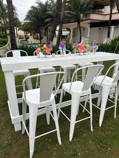 a white table and chairs sitting on top of a grass covered field next to palm trees