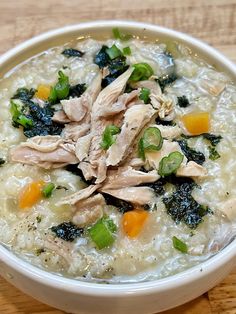 a white bowl filled with chicken and rice soup on top of a wooden table next to a spoon