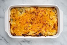 a casserole dish with cheese and vegetables in it on a marble countertop