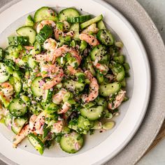 a white plate topped with cucumber and shrimp salad on top of a table