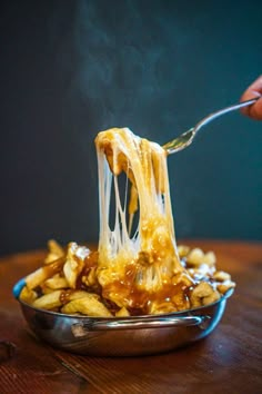 a spoonful of food is being lifted from a bowl with french fries on it