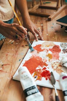 a person painting on a piece of paper with paintbrushes and watercolors