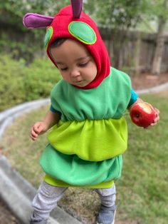 a small child in a green and red dress holding an apple while standing on some steps