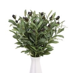 a white vase filled with lots of green leaves and olives on top of a table